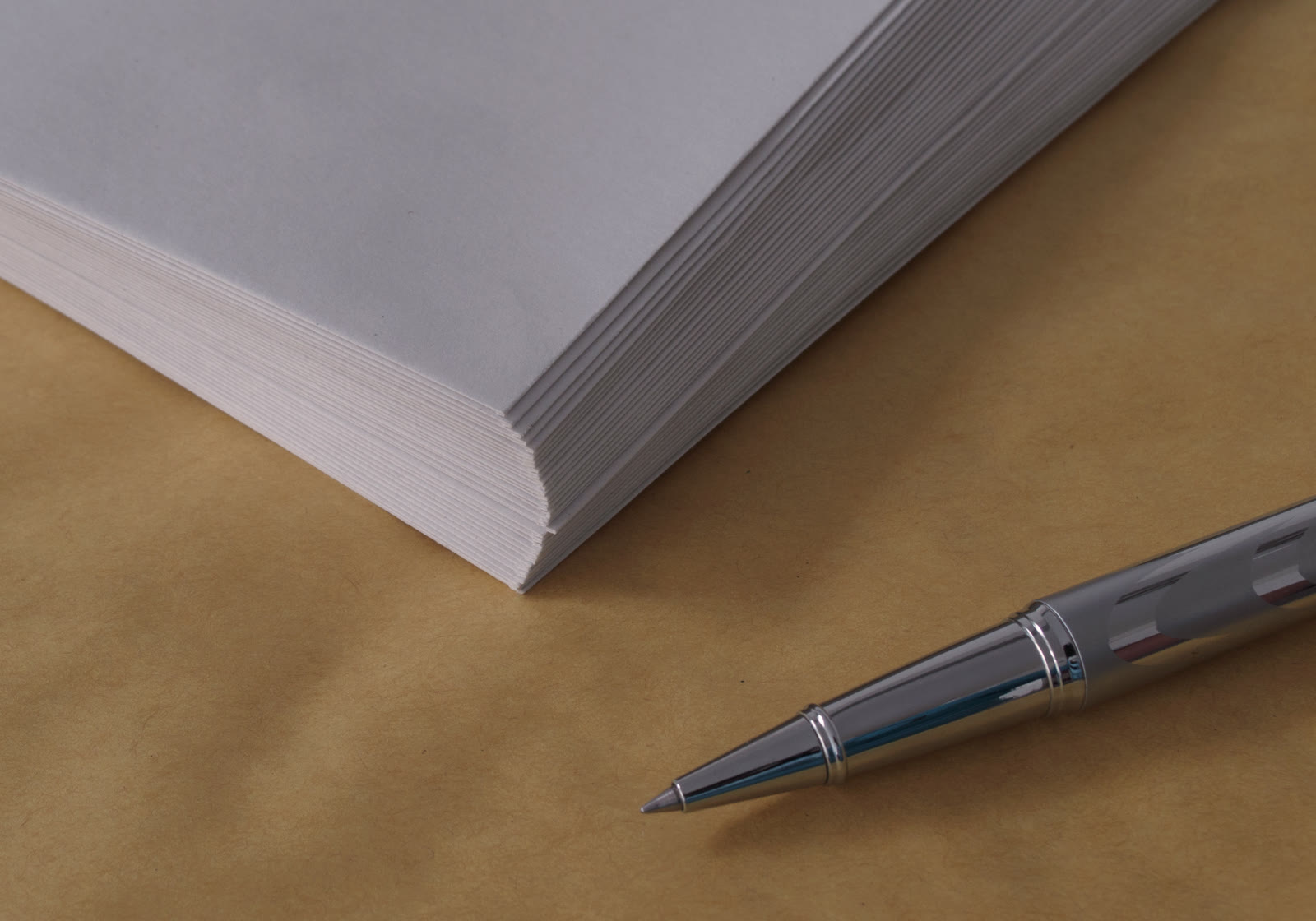 Pilha de papel branco e uma caneta sobre papel pardo