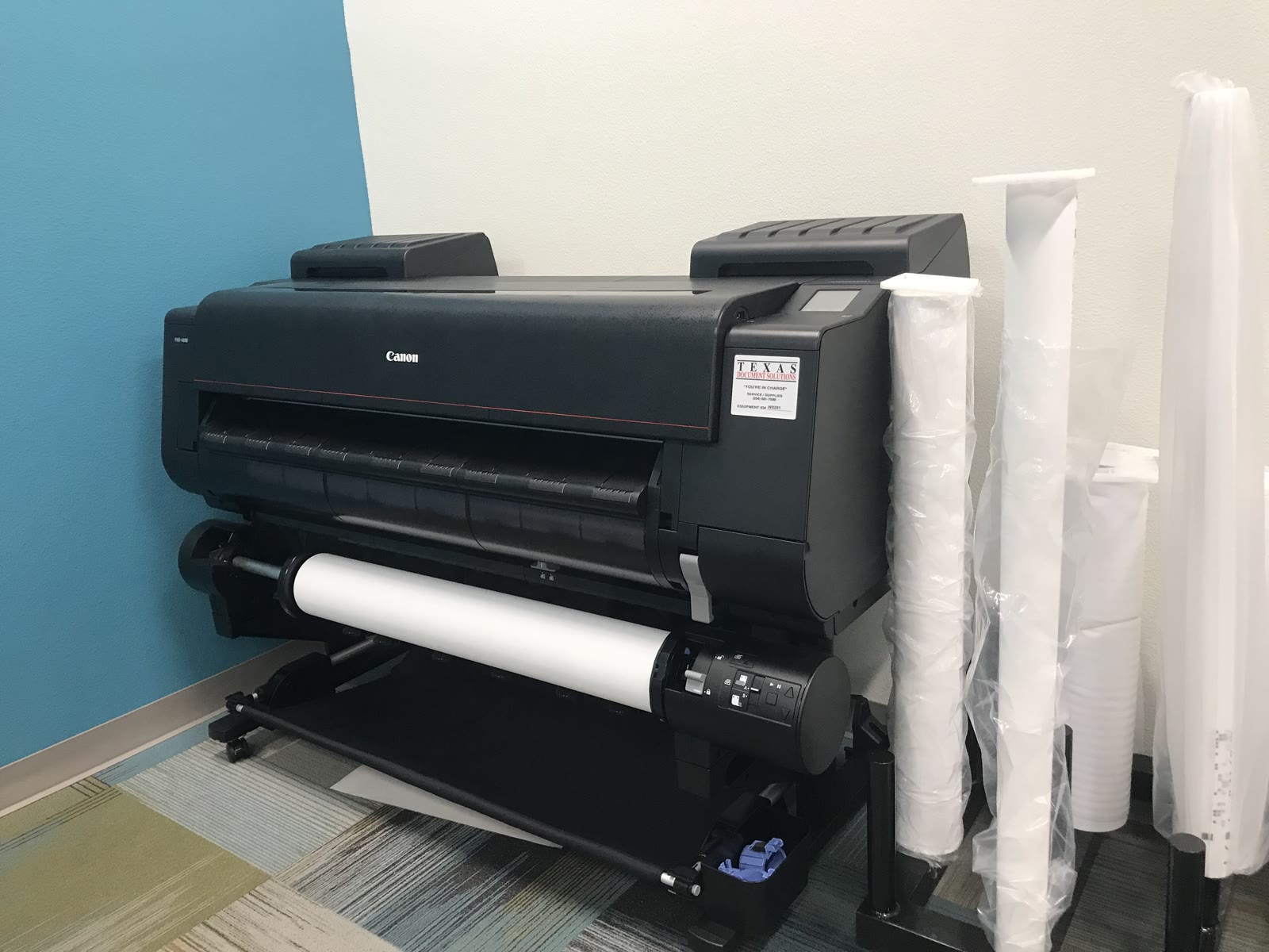 Plotter com rolo de papel e bobinas encostadas na parede