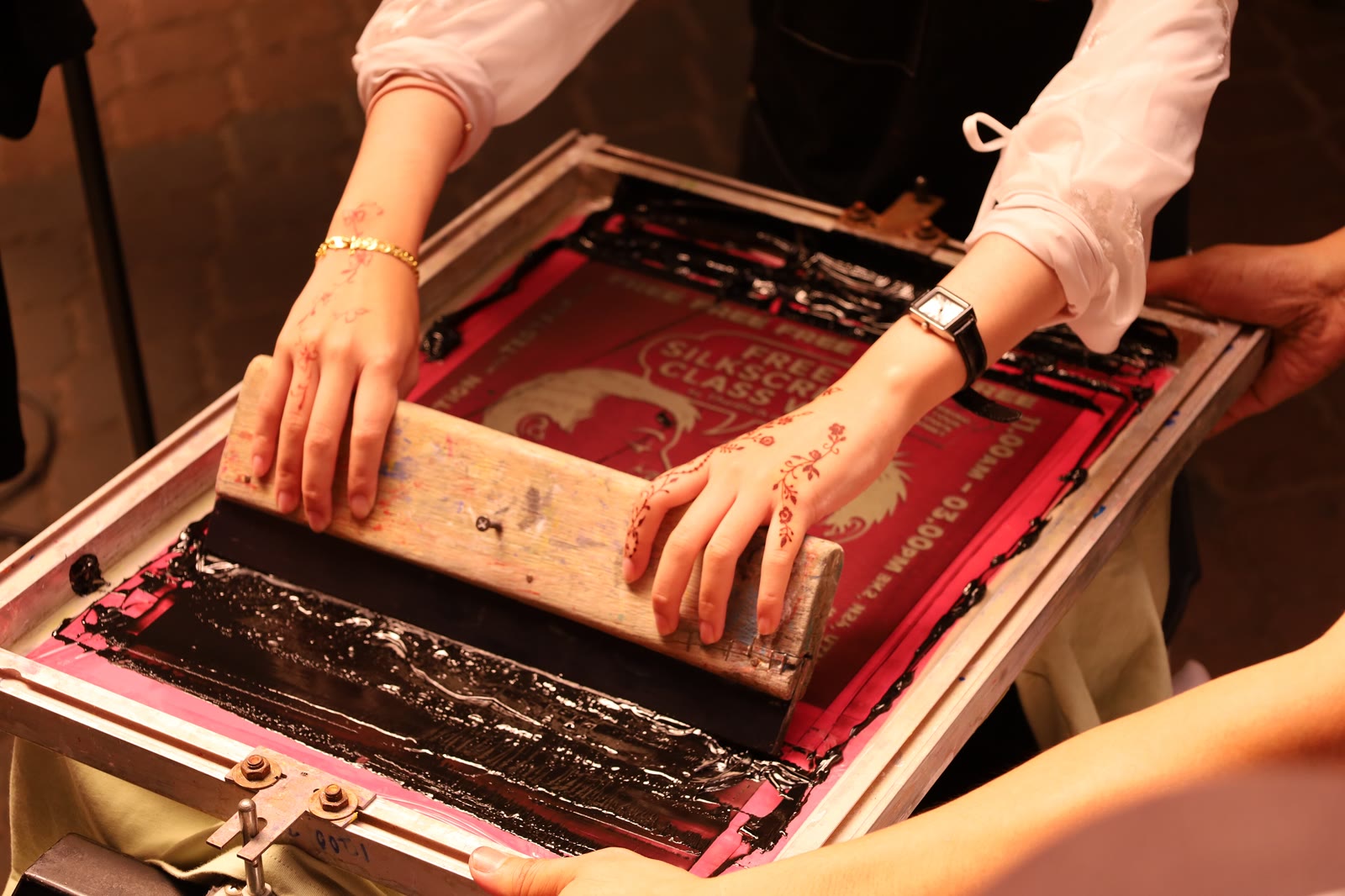 Mãos puxando a tinta numa tela de serigrafia